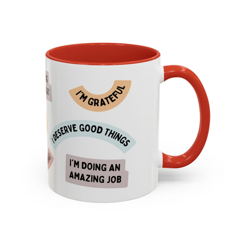 White ceramic mug with orange handle and interior featuring motivational affirmations like I’m grateful, I deserve good things, and I’m doing an amazing job.